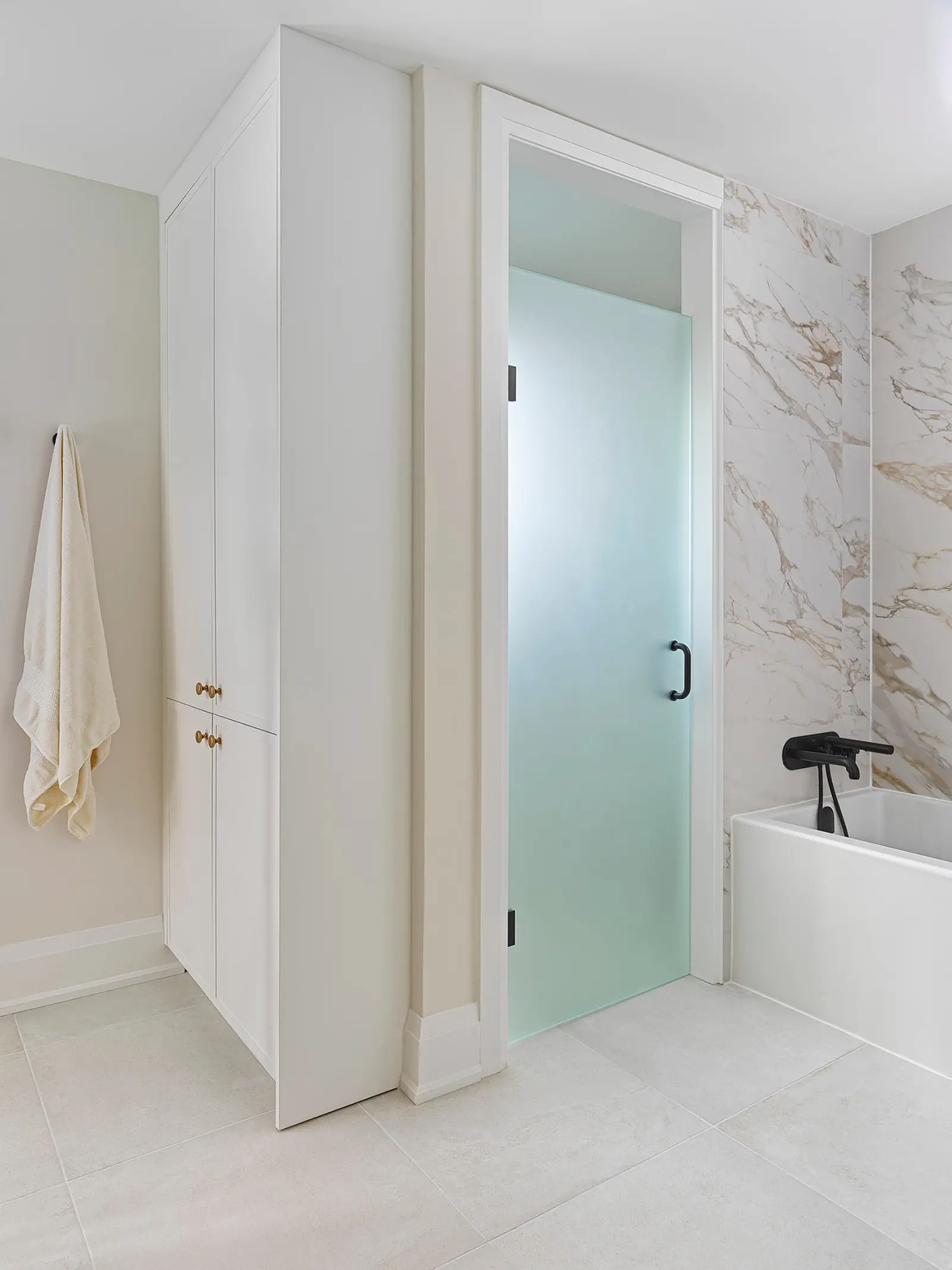 Frosted glass shower door beside a built-in linen cabinet