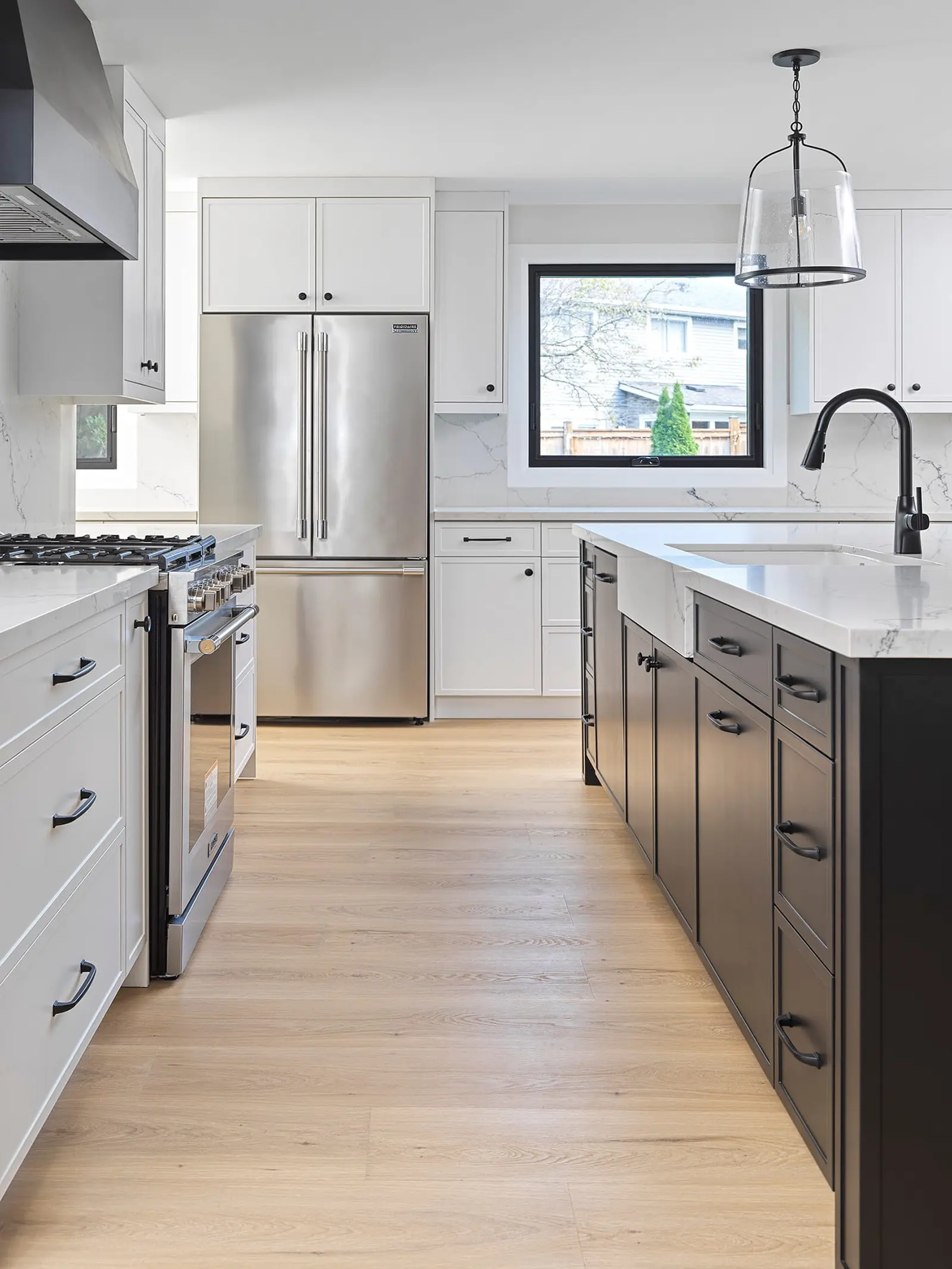 White kitchen with a black island, gas range and stainless fridge
