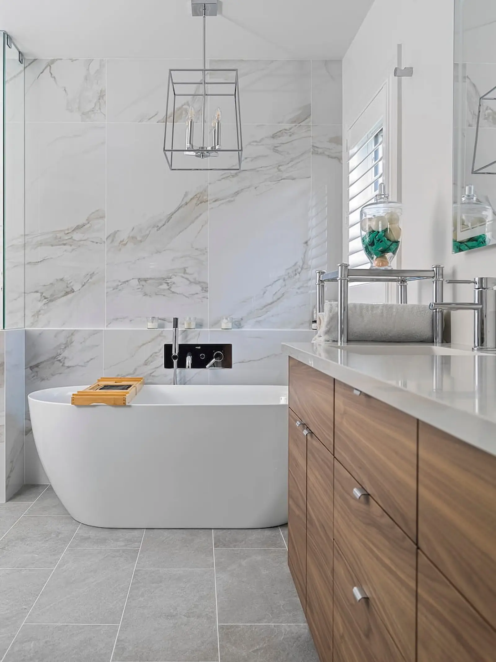 Freestanding tub beside a wood vanity and marble-look tile wall