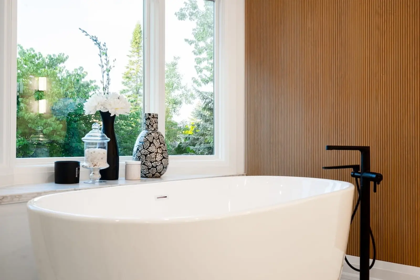 Freestanding tub with a black filler and wood slat wall