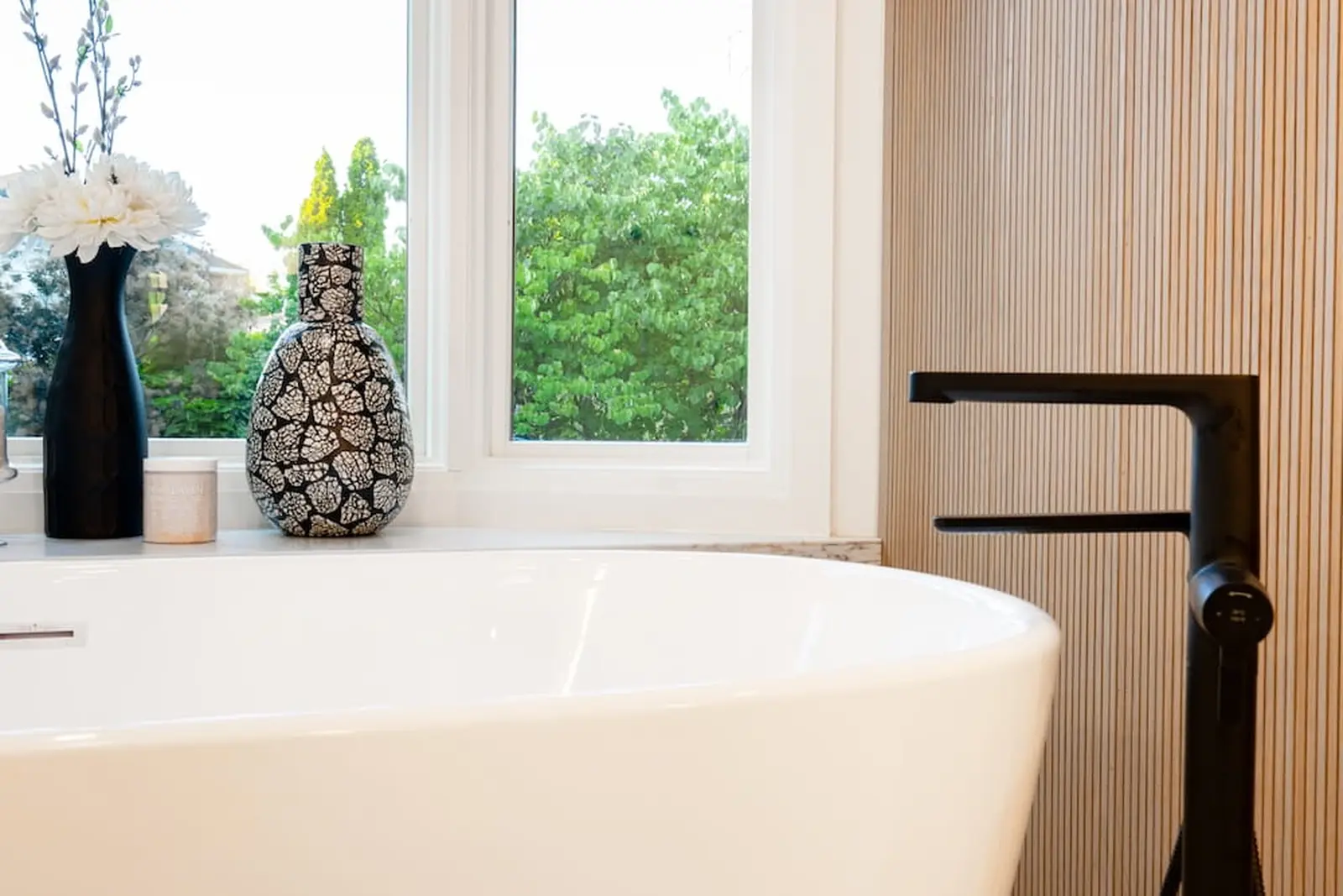 Black tub filler beside a freestanding tub and wood slat wall