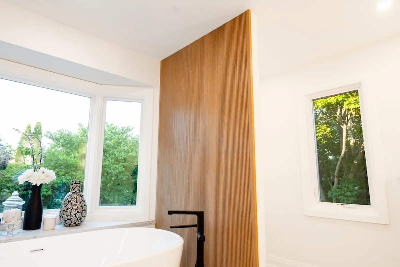 Freestanding tub framed by a window and wood slat feature wall