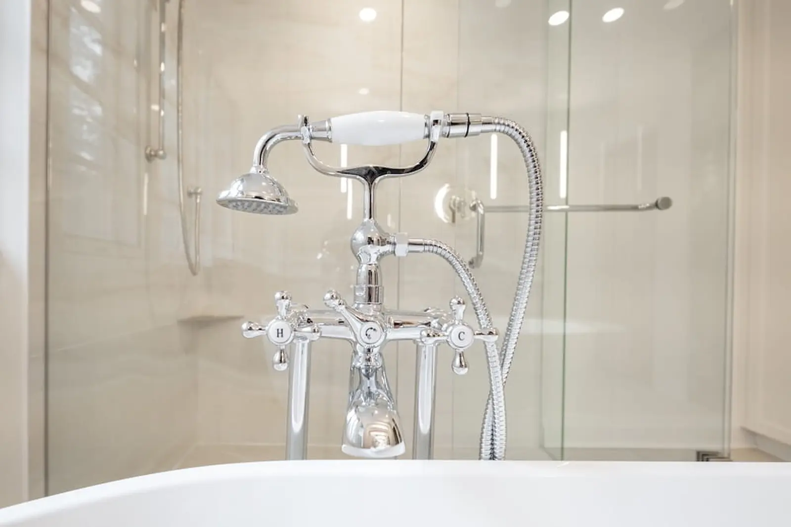 Telephone-style tub filler with a hand shower beside a glass enclosure