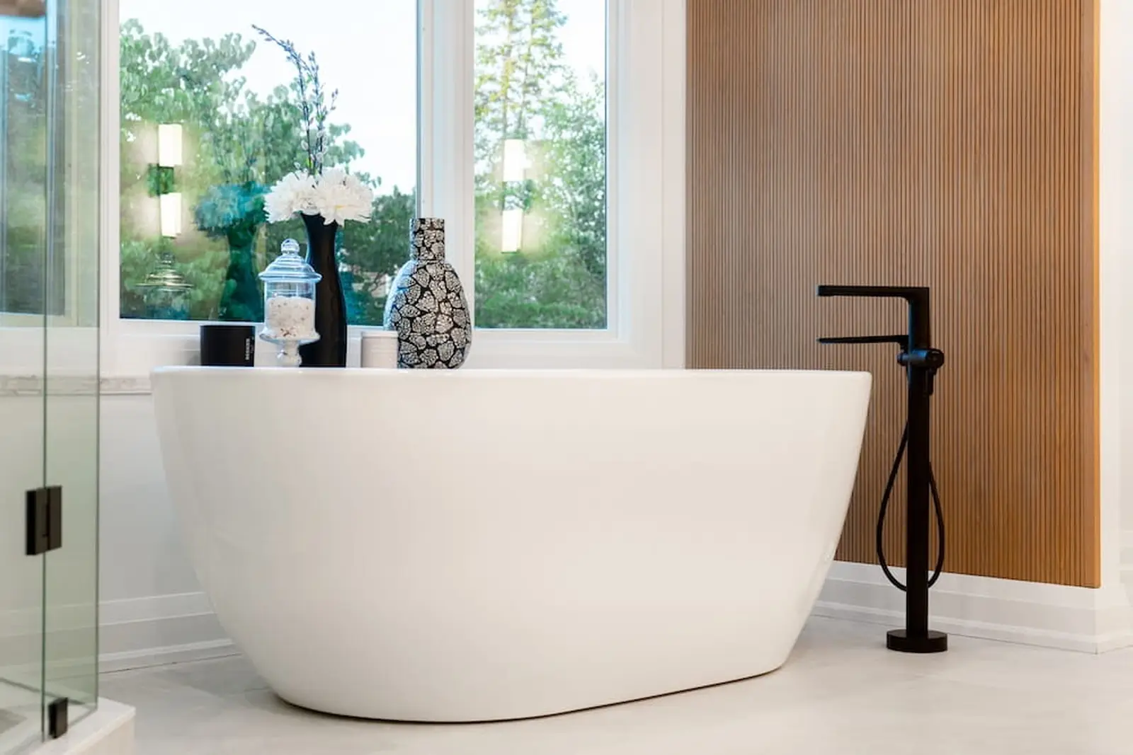 Freestanding tub with a black floor-mounted filler beside a window