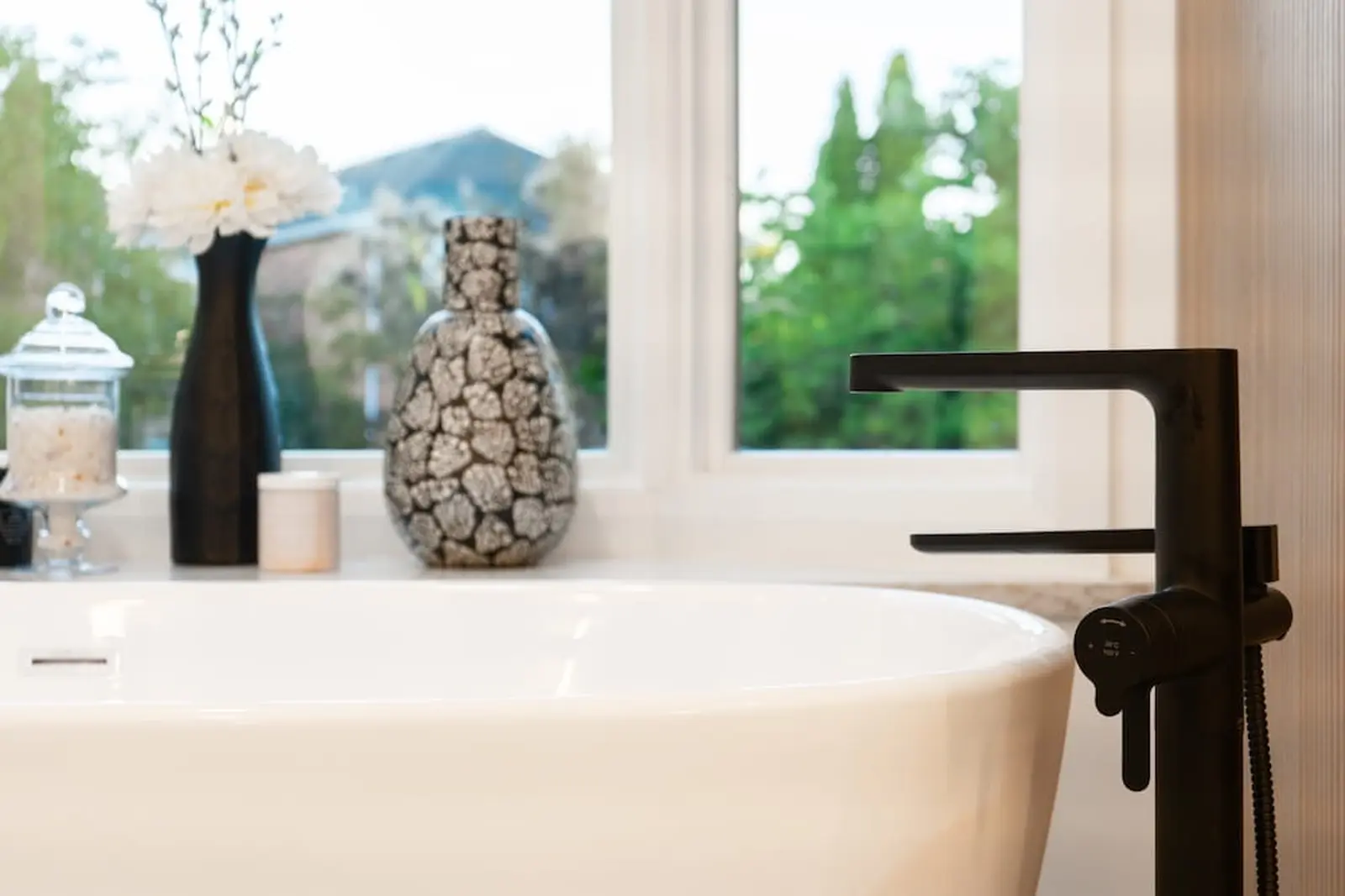 Freestanding tub with black fixtures beside a window