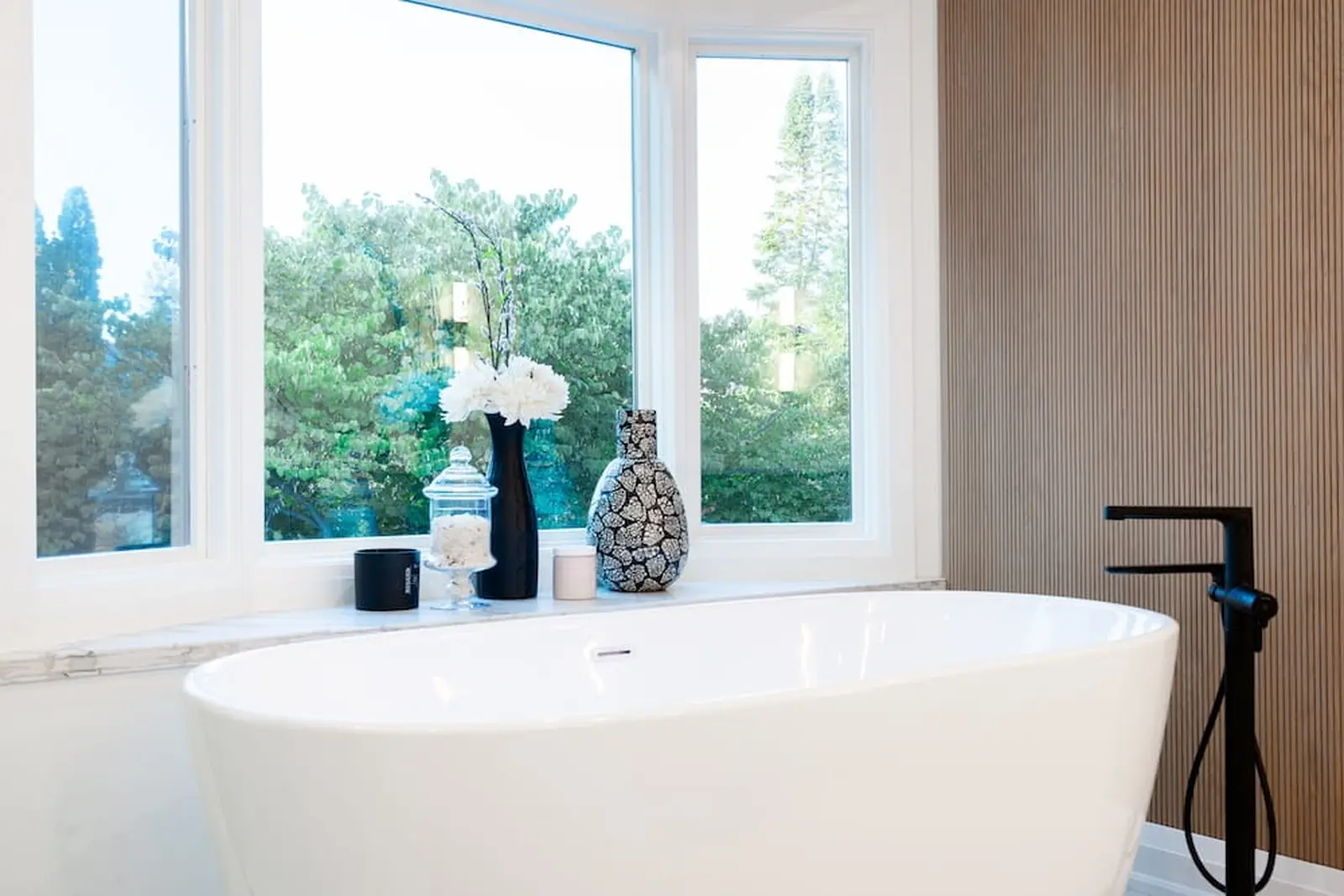 Freestanding soaker tub under a window with black fixtures