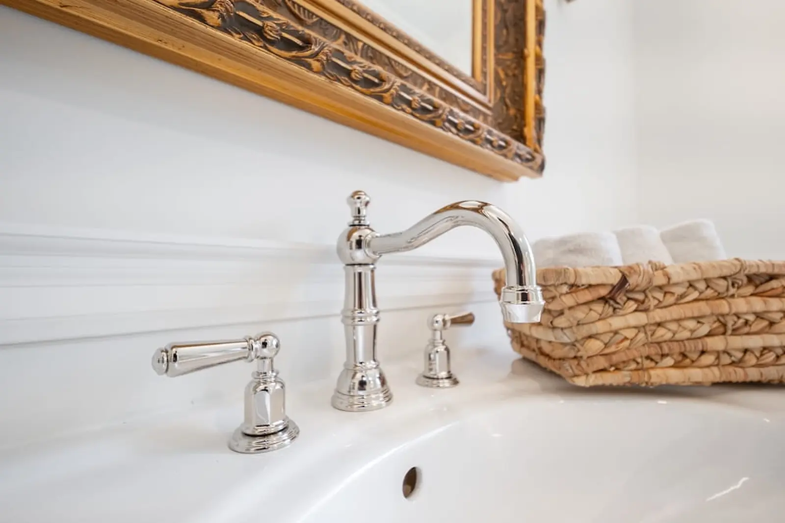 Polished nickel faucet on a white sink beneath an ornate mirror