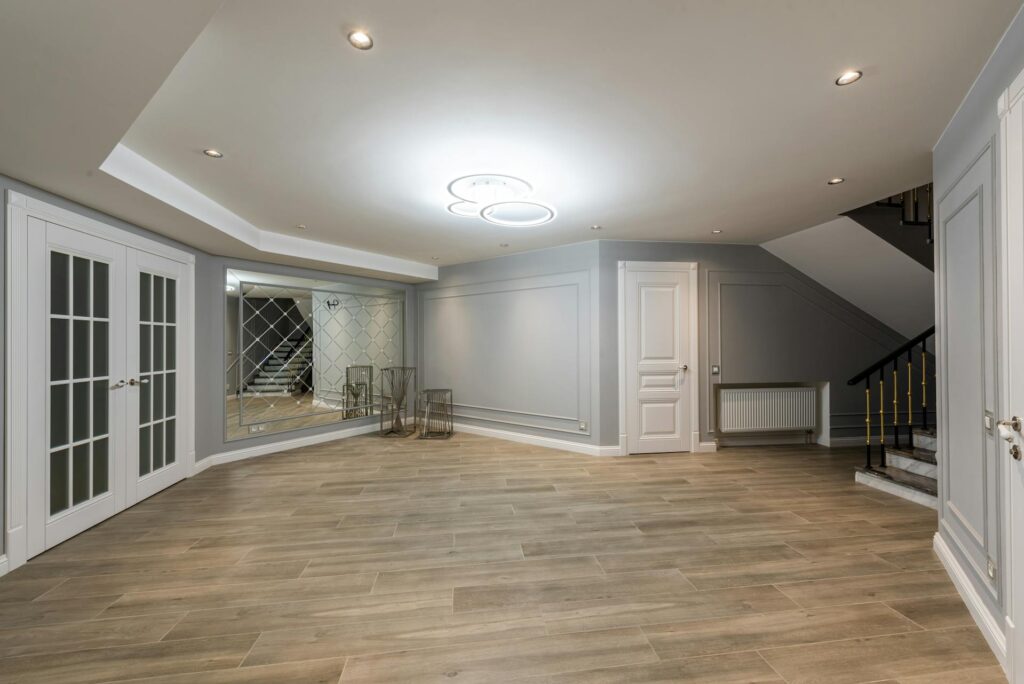 Finished basement recreation room with light flooring and pot lights