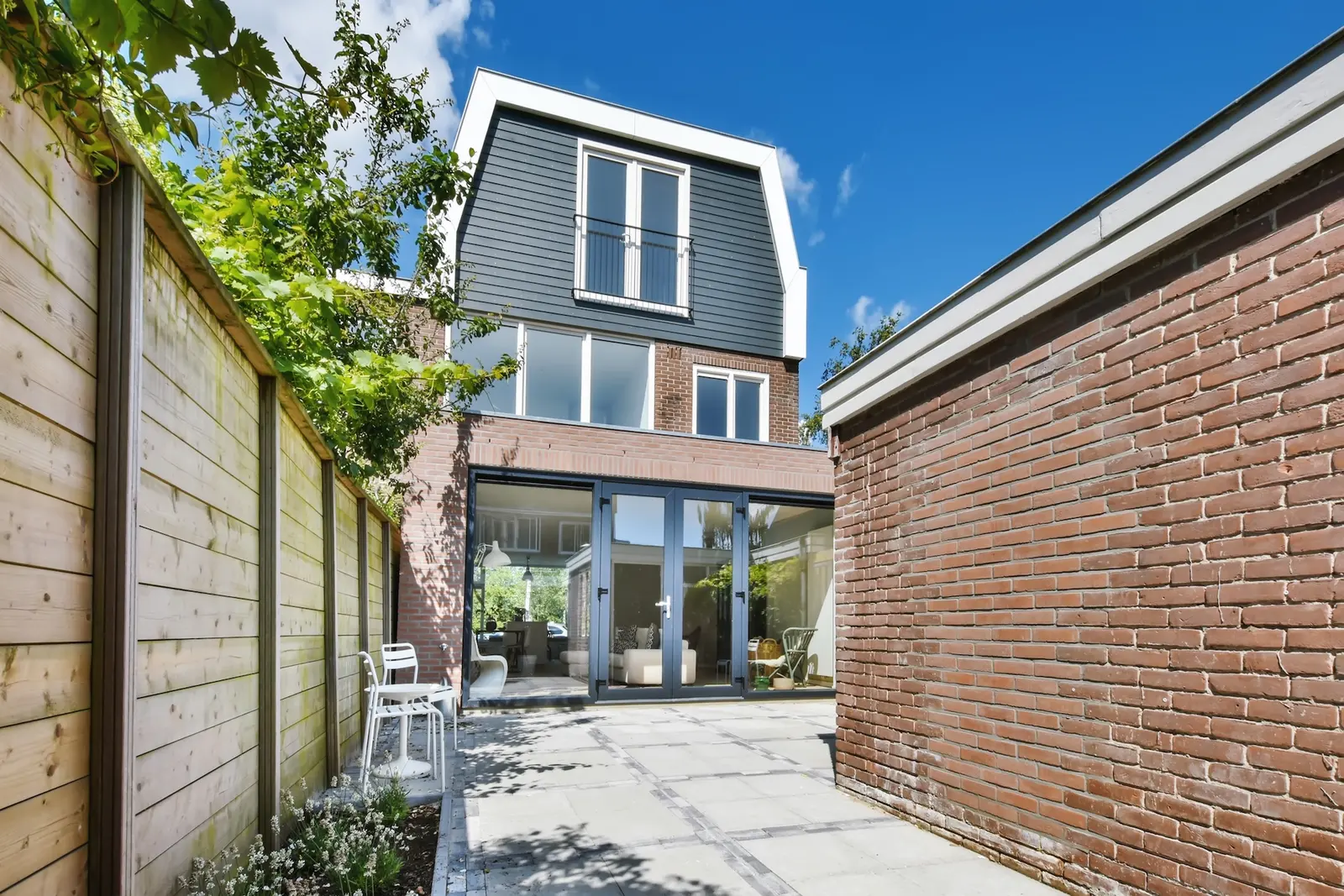 Narrow-lot backyard home with glass doors opening onto a paved patio