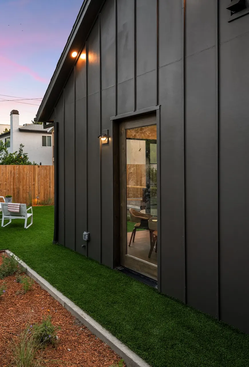 Dark board-and-batten backyard suite beside a landscaped yard at dusk